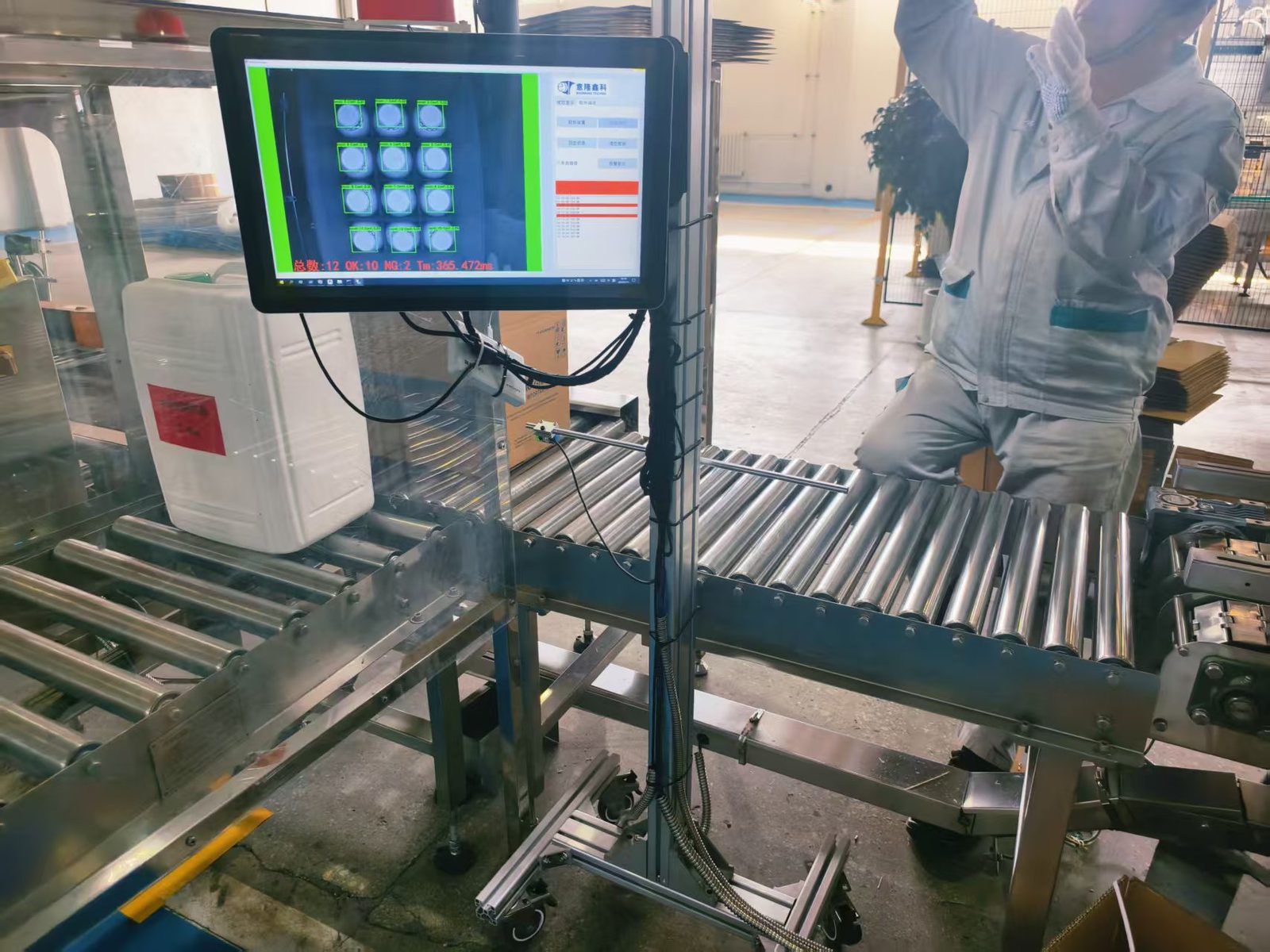 Operator at a cap inspection station: monitor showing a grid of caps with green region-of-interest overlays over a roller conveyor